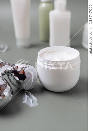 Metal facial roller with moisturizing skincare cream and cosmetic jar on neutral background, beauty treatment concept Metal facial roller with moisturizing skincare cream and cosmetic jar on neutral background, beauty treatment concept 138747092