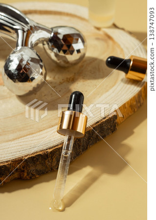 Facial massage roller and cosmetic serum dropper bottle on wooden slice with warm sunlight, skincare beauty concept 138747093