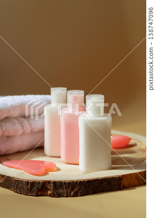 Skincare cosmetic bottles with facial gua sha and towel on wooden slice in warm sunlight, beauty routine concept 138747096