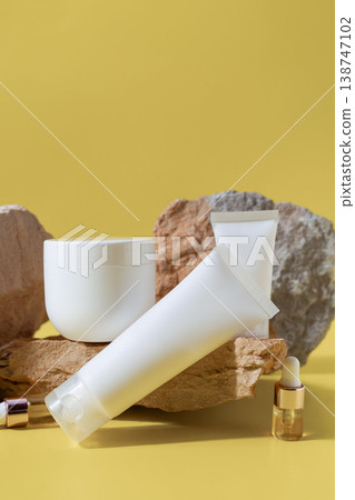 Collection of skincare cosmetic bottles, tubes and serum dropper arranged on natural stones on yellow background, beauty product display 138747102