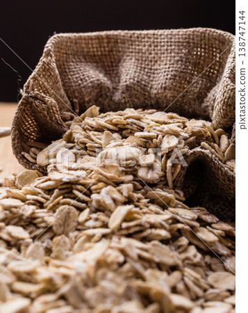 oat flakes cereal in burlap sack on wooden table. oat flakes cereal in burlap sack on wooden table. 138747144