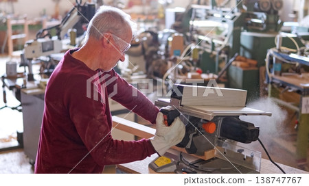 Experienced woodworker sawing wood with miter saw in workshop Experienced woodworker sawing wood with miter saw in workshop 138747767