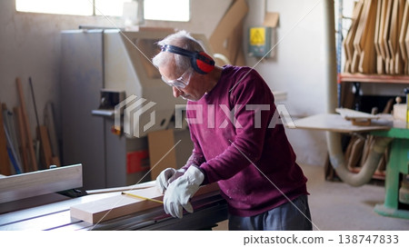 Senior carpenter measuring wood in safety gear with pencil Senior carpenter measuring wood in safety gear with pencil 138747833