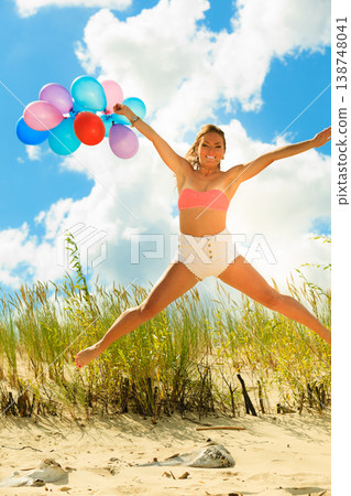 Girl jumping with colorful balloons on beach Girl jumping with colorful balloons on beach 138748041