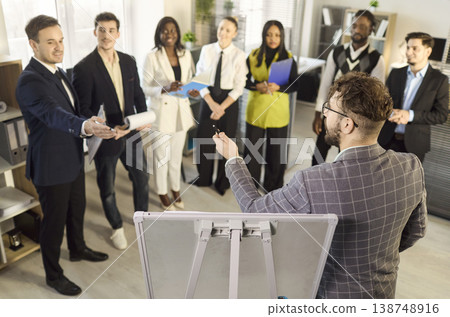 Business team in office workshop with male presenter engaging colleagues standing 138748916