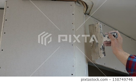 A spatula in the hand of a person repairing a room wall under the ceiling near a rounded corner and a doorway, filling holes during the installation of a room partition 138749746