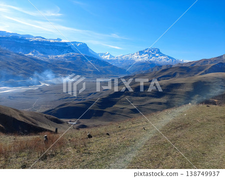 Valley with dry grass and snow-covered peaks under sunny blue sky Valley with dry grass and snow-covered peaks under sunny blue sky 138749937