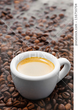 Freshly brewed espresso in a white cup, rich crema forming on top, surrounded by roasted coffee beans with steam rising 138750704