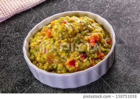 Fresh homemade guacamole in a white bowl with avocado and red chili pepper ingredients on a dark background Fresh homemade guacamole in a white bowl with avocado and red chili pepper ingredients on a dark background 138751038