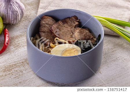 Bowl of authentic ramen noodle soup with pork, boiled egg, and fresh ingredients on a textured table Bowl of authentic ramen noodle soup with pork, boiled egg, and fresh ingredients on a textured table 138751417