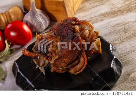 Delicious roasted pork knuckle with crispy skin served on a black plate with fresh garlic and tomatoes Delicious roasted pork knuckle with crispy skin served on a black plate with fresh garlic and tomatoes 138751481