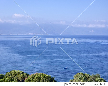 Picturesque view to blue sea and mountain island on horizon in mist. Calm water surface, background for traveling and vacation,Beautiful sea view, sailboats far away in the sea in sunny day. Picturesque view to blue sea and mountain island on horizon in mist. Calm water surface, background for traveling and vacation,Beautiful sea view, sailboats far away in the sea in sunny day. 138751691