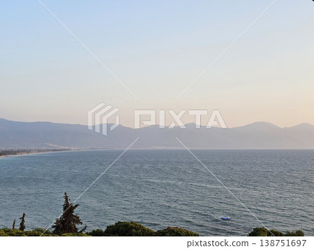 Picturesque view to blue sea and mountain island on horizon in mist. Calm water surface, background for traveling and vacation,Beautiful sea view, sailboats far away in the sea in sunny day. Picturesque view to blue sea and mountain island on horizon in mist. Calm water surface, background for traveling and vacation,Beautiful sea view, sailboats far away in the sea in sunny day. 138751697