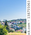Scenic view of a hillside town with residential buildings and greenery under a clear blue sky in a vibrant urban landscape 138755063