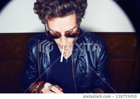 Man with cigarette, punk in sunglasses and rockstar attitude on white background with spotlight. Cool rock style, grunge fashion and smoking, confident and handsome male model in studio with freedom. 138755450