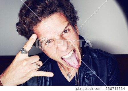 Rockstar man, horns and hand in studio for emoji in spotlight, fashion or leather jacket by background. Person, symbol and icon by halo for portrait, punk style and tongue with jewelry for aesthetic Rockstar man, horns and hand in studio for emoji in spotlight, fashion or leather jacket by background. Person, symbol and icon by halo for portrait, punk style and tongue with jewelry for aesthetic 138755534