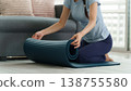 Asian adult woman rolls up yoga mat home living room preparing fitness wellness exercise healthy lifestyle workout 138755580