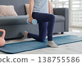 Asian adult exerciser performing dumbbell lunges on yoga mat for fitness training at home living room for strength wellness 138755586
