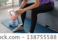 Asian woman hydrating home workout taking break after exercise session sitting on sofa holding water bottle practicing fitness wellness lifestyle at home 138755588
