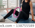 Adult Asian woman performs pilates ring thigh squeeze exercise home workout for core strength and body toning indoors fitness routine wellness activity 138755589