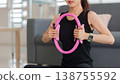 Asian adult woman performing pilates ring exercise home workout for core strength wellness indoor living room fitness session healthy lifestyle body training 138755592