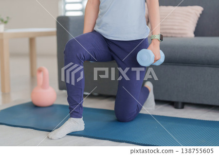 Adult Asian woman home workout strength training using dumbbell practicing lunge exercise at living room floor for fitness health body muscle gain Adult Asian woman home workout strength training using dumbbell practicing lunge exercise at living room floor for fitness health body muscle gain 138755605