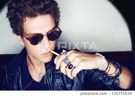 Portrait of man with cigarette, rock fashion and rockstar attitude on white background in spotlight. Cool punk style, grunge and smoking, confident and handsome male model in studio with sunglasses 138755634