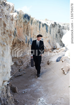 Travel, briefcase and business man at a beach for thinking, reflection or enjoying break outdoor. Nature, rock and young male entrepreneur walking in a suit for fresh air, getaway or peaceful morning 138756078