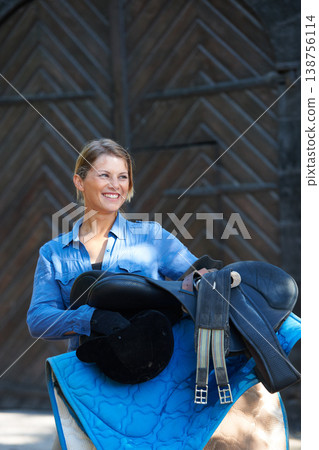 Saddle, ready or happy woman in countryside outdoor with rider or jockey for recreation or wellness. Sports, horse riding tools or equestrian with gear to start training, exercise or workout in ranch 138756114