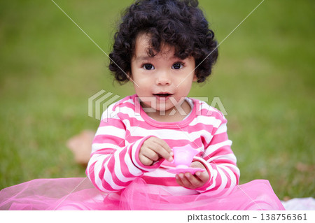 Nature, portrait and girl kid in a garden play with toy on the grass on summer weekend. Adorable, playful and young child, baby or toddler with curly hair sitting on the lawn in outdoor field or park Nature, portrait and girl kid in a garden play with toy on the grass on summer weekend. Adorable, playful and young child, baby or toddler with curly hair sitting on the lawn in outdoor field or park 138756361