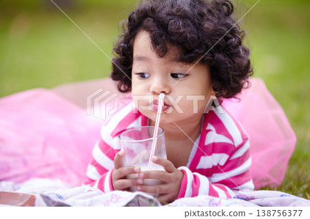 Girl, child and drinking of milk on grass with straw in pink tutu while lying for picnic. Youth, curly hair and kid with dairy for balanced diet, nutrition and calcium for development of strong bones 138756377