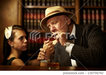 Mafia, boss and man with cigarette in office, woman and light for smoking. Mature person, godfather and hat in suit for power, reputation and career for criminal activity with tobacco for relaxation Mafia, boss and man with cigarette in office, woman and light for smoking. Mature person, godfather and hat in suit for power, reputation and career for criminal activity with tobacco for relaxation 138756742