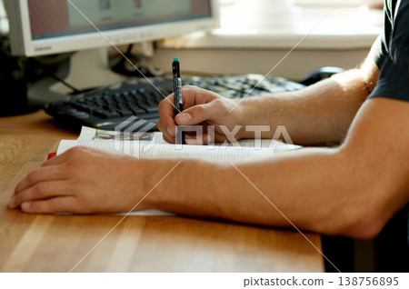 Hands, education and a pen for homework with a person at a desk in their home for learning or development. Study, writing and book with a student closeup in an apartment for university research 138756895