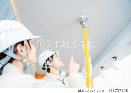 A man and a woman in work clothes inspecting an automatic fire alarm system. A man and a woman in work clothes inspecting an automatic fire alarm system. 138757308