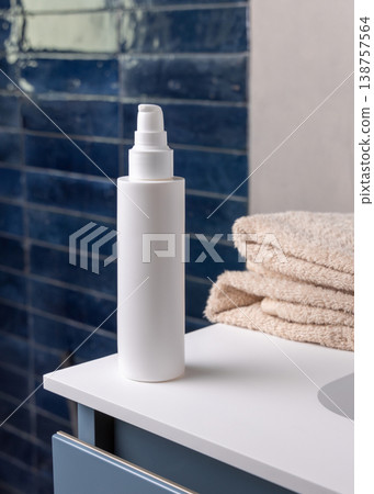 White pump cosmetic bottle near beige bath towel in dark blue bathroom, cosmetic mockup 138757564