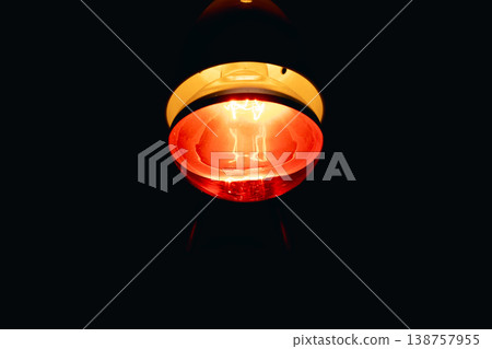 A red infrared lamp for medical therapy that emits intense heat in a dark environment and infrared light with a golden orange glow. A red infrared lamp for medical therapy that emits intense heat in a dark environment and infrared light with a golden orange glow. 138757955