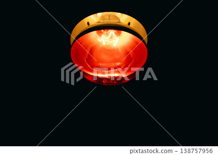 A red infrared lamp for medical therapy that emits intense heat in a dark environment and infrared light with a golden orange glow. A red infrared lamp for medical therapy that emits intense heat in a dark environment and infrared light with a golden orange glow. 138757956
