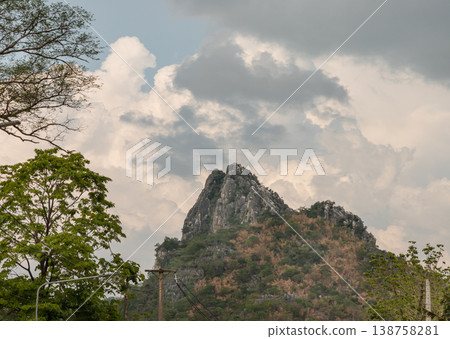 The mountain stony, grey spine cuts through the verdant forest, standing as a silent sentinel against the elements. In the foreground, the foliage glows with life, contrasting with the soft, The mountain stony, grey spine cuts through the verdant forest, standing as a silent sentinel against the elements. In the foreground, the foliage glows with life, contrasting with the soft, 138758281