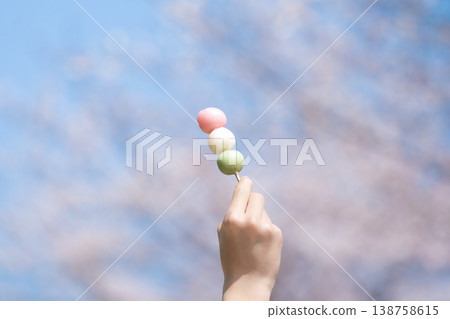 一張照片中，有人手持三色團子（糯米糰子），背景是櫻花，讓人聯想到「花上團子」的意象。 138758615