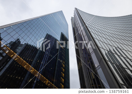 Looking up at towering glass office buildings against a cloudy sky Looking up at towering glass office buildings against a cloudy sky 138759161