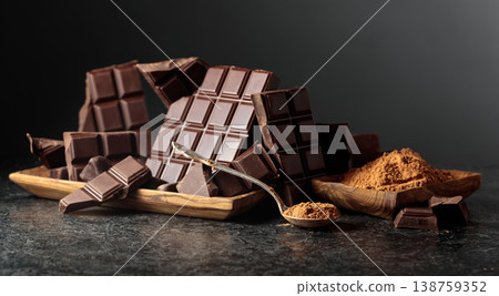 Broken dark chocolate bar and cocoa powder on a black background. Broken dark chocolate bar and cocoa powder on a black background. 138759352