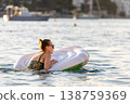 Woman wear green swimsuit relax inflatable ring calm sea near yachts forested coast sunset warm summer sunlight. Female person peaceful moment  leisure freedom vacation lifestyle serene getaway mood 138759369