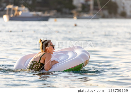 Woman wear green swimsuit relax inflatable ring calm sea near yachts forested coast sunset warm summer sunlight. Female person peaceful moment leisure freedom vacation lifestyle serene getaway mood Woman wear green swimsuit relax inflatable ring calm sea near yachts forested coast sunset warm summer sunlight. Female person peaceful moment leisure freedom vacation lifestyle serene getaway mood 138759369