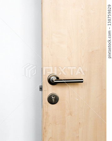 Wooden door in room, surface with smooth finish. Metal handle, keyhole for locking. Simple design against plain wall. Natural light illuminates room, interior, closeup Wooden door in room, surface with smooth finish. Metal handle, keyhole for locking. Simple design against plain wall. Natural light illuminates room, interior, closeup 138759829
