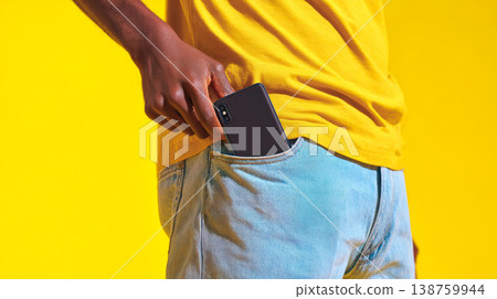 Person slips smartphone into front pocket of light blue jeans and a mustard t-shirt 138759944