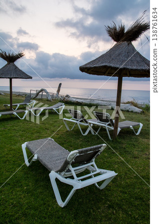Thatched-roof parasols and beach beds line the coast at dawn on the French island of Corsica in the Mediterranean Sea. Thatched-roof parasols and beach beds line the coast at dawn on the French island of Corsica in the Mediterranean Sea. 138761634