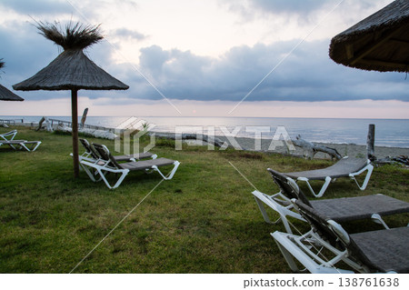 在地中海的法國科西嘉島，黎明時分，茅草屋頂的遮陽傘和沙灘床沿著海岸線排列。 138761638