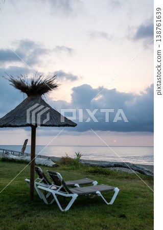 在地中海的法國科西嘉島,黎明時分,茅草屋頂的遮陽傘和沙灘床沿著海岸線排列。 在地中海的法國科西嘉島,黎明時分,茅草屋頂的遮陽傘和沙灘床沿著海岸線排列。 138761639