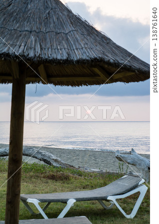 在地中海的法國科西嘉島,黎明時分,茅草屋頂的遮陽傘和沙灘床沿著海岸線排列。 在地中海的法國科西嘉島,黎明時分,茅草屋頂的遮陽傘和沙灘床沿著海岸線排列。 138761640