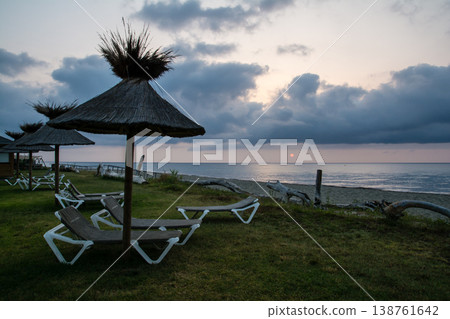 Thatched-roof parasols and beach beds line the coast at dawn on the French island of Corsica in the Mediterranean Sea. Thatched-roof parasols and beach beds line the coast at dawn on the French island of Corsica in the Mediterranean Sea. 138761642